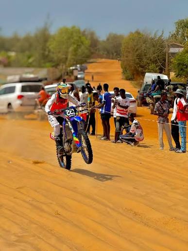 Pilote de moto-cross franchissant une bosse sur un circuit sablonneux