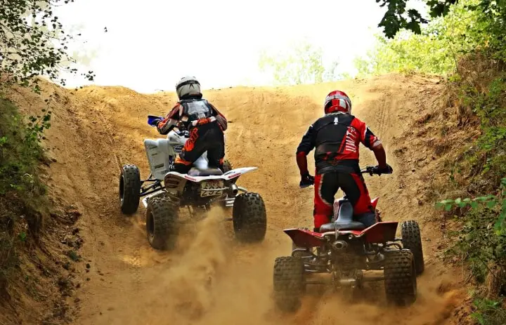Deux pilotes en quads sportifs sur une montée de piste sablonneuse