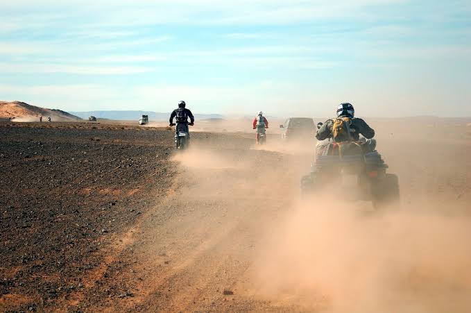 Pilotes en quad et moto avançant sur une grande piste sablonneuse