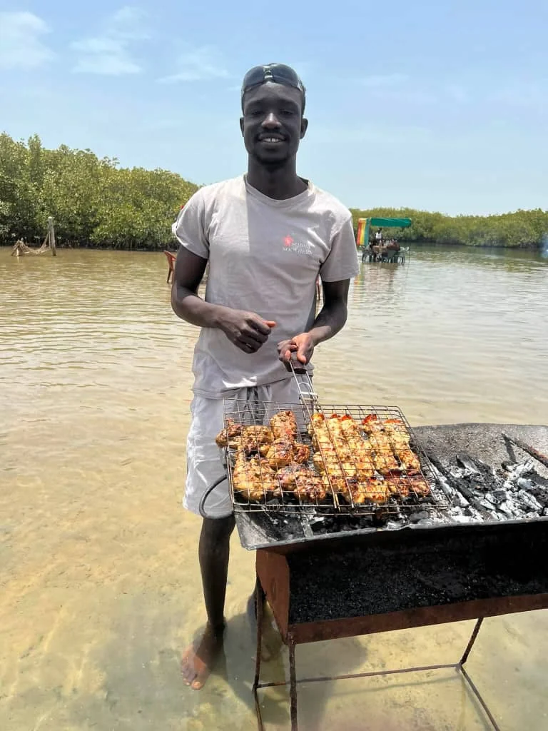 Guide local préparant le déjeuner grillé pendant la journée découverte de Mar Lodj au Sine Saloum